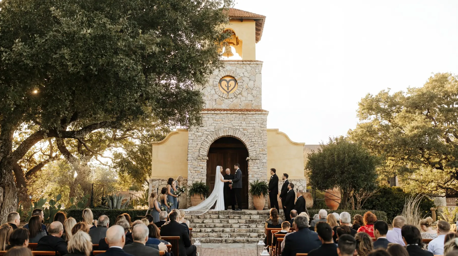 Outdoor ceremony at a Hill Country stone chapel, guests seated under live oaks