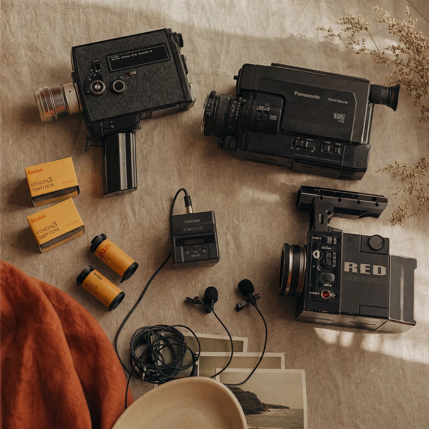 Super 8 camera, VHS camcorder, Kodak film cartridges, lav mics, and a RED cinema camera laid out on linen